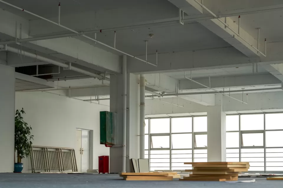 Vacant interior of open plan office with large buildings and stacked wood planks on floor.